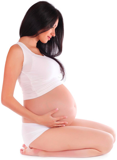 Femme enceinte aux cheveux noirs tenant son ventre, assise en tailleur